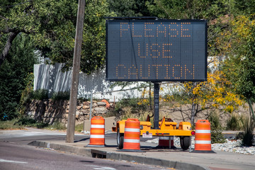 Solar mobile sign with orange cones sitting on sidewalk besides road saying Please Use Caution - Selective focus