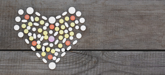 Colorful pills arranged in heart shape on wooden background.