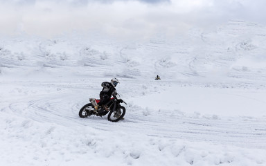 Biker motorcyclist riding on snow and ice in cold winter day. Extreme winter sport. 