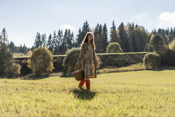 Young woman with long red hair in a linen dress gathering mushrooms in the forest in the bast basket