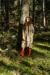 Young woman with long red hair in a linen dress gathering mushrooms in the forest in the bast basket