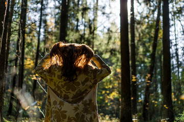 Young woman with long red hair in a linen dress gathering mushrooms in the forest in the bast basket