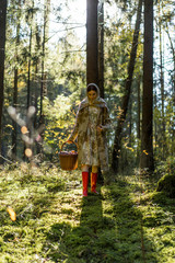 Young woman with long red hair in a linen dress gathering mushrooms in the forest in the bast basket