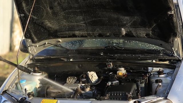 Young attractive man perfusing with water his silver car