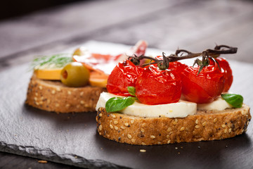 Fototapeta na wymiar Bruschettas with cream cheese, cherry tomato, basil, smoked cheese, prosciutto, olives on wooden table