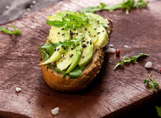Bruschetta with avocado, rucola sesame and seeds on wooden table