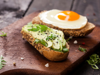 Two different bruschettas with avocado, rucola sesame, seeds, egg on wooden table