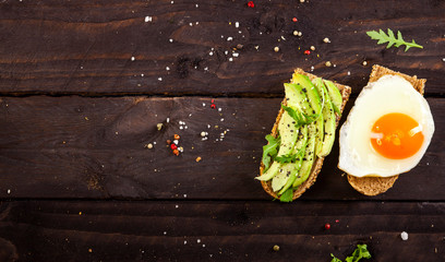 Two different bruschettas with avocado, rucola sesame, seeds, egg on wooden table