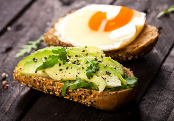 Two different bruschettas with avocado, rucola sesame, seeds, egg on wooden table