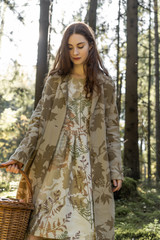 Young woman with long red hair in a linen dress gathering mushrooms in the forest in the bast basket