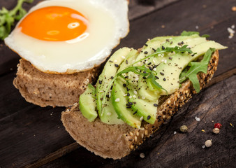 Two different bruschettas with avocado, rucola sesame, seeds, egg on wooden table