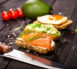 Three different bruschettas with avocado, rucola sesame, seeds, egg, salmon on wooden table