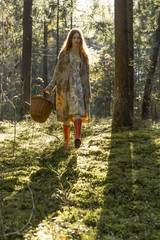 Young woman with long red hair in a linen dress gathering mushrooms in the forest in the bast basket