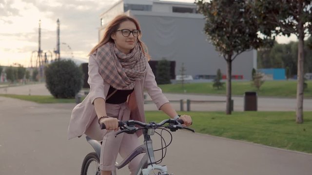 Happy teenager girl is driving a bike in a park in twilight