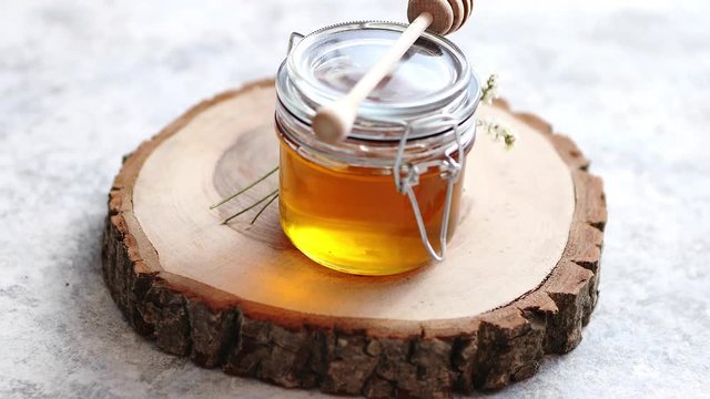 Glass jar full of fresh honey placed on slice of wood. Stone background with copy space.
