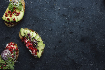 Healthy avocado sandwiches with avocado slices, seeds and sprouts on dark background with copy space.
