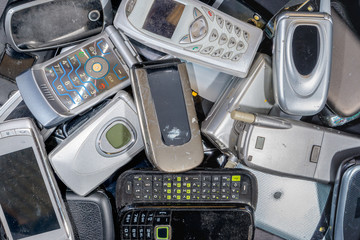 A pile of old cell phones to be recycled. There are a variety of phones, but most are the flip to...