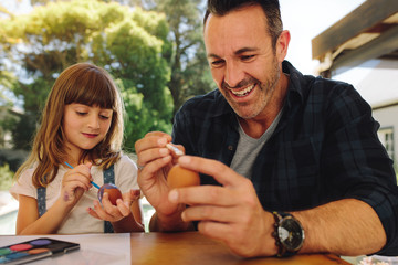 Father and daughter putting paint on easter eggs