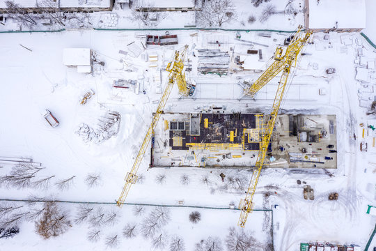 yellow tower cranes working at city construction site in winter under snow. aerial top view