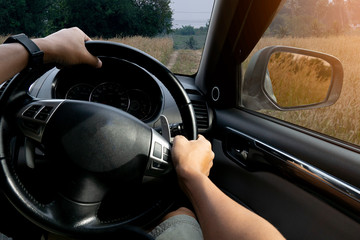 Inside view of man controls the car on a rural dirt road with grass covered throughout the route.