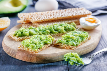 Rye, wheat crisp bread with avocado and egg on wooden background. Crisp and avocado sandwich.