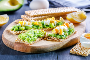 Rye, wheat crisp bread with avocado and egg on wooden background. Crisp and avocado sandwich.
