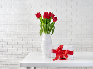Red tulips in white vase next to a gift box with red ribbon