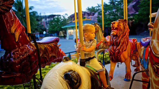 Cute boy riding on the carousel in the amusement park