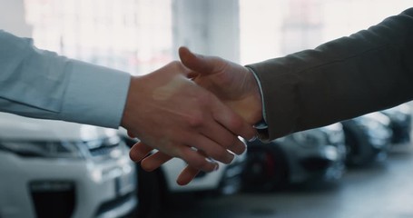 Close up of dealer and new owner handshake after concluding a car deal in auto show or salon. Slow motion shot in 8K. Concept of car dealerships, used cars, car sale and rent, auto deal