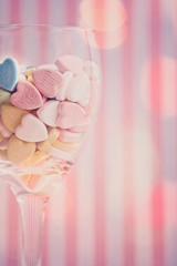 Wine glass filled with pastel valentine love message candies on a stripped pink background