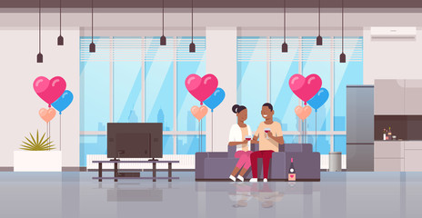 couple drinking wine happy valentines day concept african american man woman lovers watching tv on couch modern apartment home interior air heart shape balloons flat horizontal