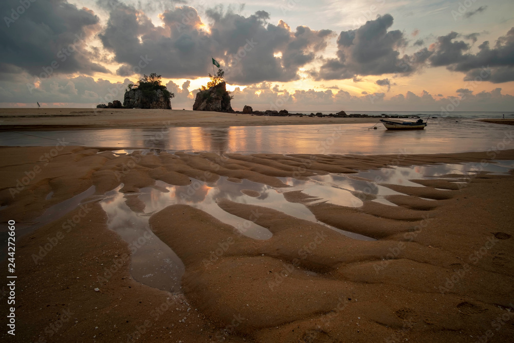 Wall mural Two standing rocks near the beach with reflection of dramatic clouds during sunrise and unique sands with stranded boat