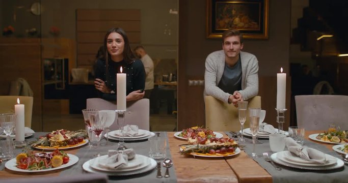 MS Caucasian couple or friends standing near the dining table, looking into camera. 4K UHD 60 FPS SLOW MOTION Blackmagic RAW