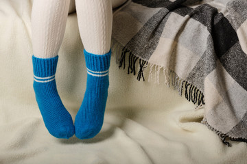 Female legs in warm white knitted tights and blue socks on a white background made of faux fur