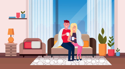 couple drinking tea man woman sitting on couch under cozy plaid happy lovers relaxing modern apartment living room interior male female characters full length horizontal