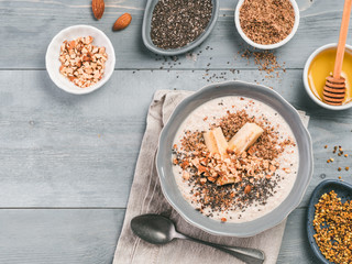 Overnight oats in bowl and ingredients - banana, LSA, chia seeds, almond, honey and pollen on gray wooden table background. Healthy breakfast oatmeal recipe idea. Top view. Copy space