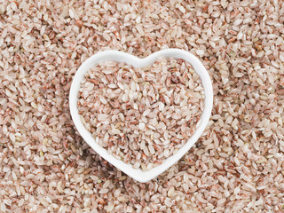 Red rice in heart-shaped bowl on rice background. Copy space. Top view or flat lay.