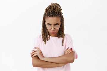 Serious-looking displeased and strict nerdy cute female with dark skin and dreads looking from...