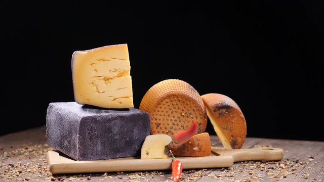 Food video. Luxury food concept. Cheese restaurant serving. Food art concept. Variety of hard cheese put on wooden board. Pods of red pepper falling down in slow motion. hd