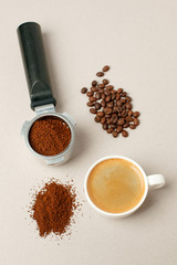 Cup of black coffee next to coffee beans and grains, handle coffee machine filter on gray background, minimal concept, closeup, Morning coffee routine