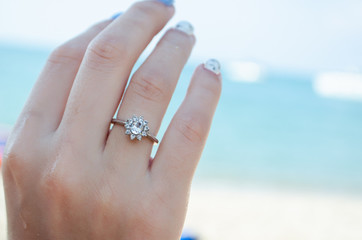 ring with a big diamond on the hand against the background of the sea and the beach