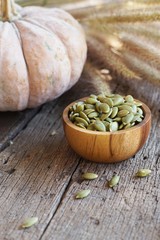 Pumpkin seed in wooden bowl and pumpkin fruit on classic wooden table background, cereal, copy space
