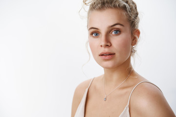 Close-up shot of woman getting ready to take-off makeup looking sensually and feminine at camera with opened lips and tender gaze standing with combed hair in light tank-top over white wall