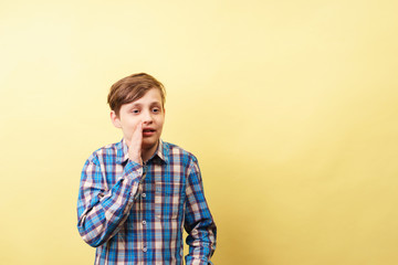 surprised startled amazed astounded and stunned boy whispering keeping hand near face over yellow...