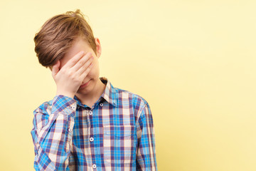 facepalm. shame and embarrassment concept. confused boy covering his face over yellow background,...