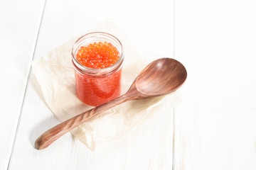 Red caviar in glass bowl and spoon on white wooden background