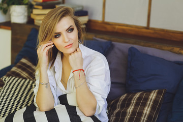 Fototapeta premium Young beautiful blonde girl in a white men's shirt on the bed