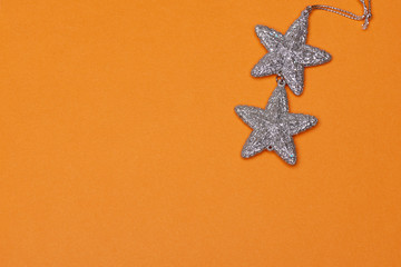 A couple of silver stars on an orange paper background with copy space for festive, Christmas and modern vibrant text.