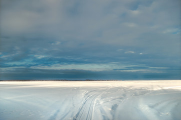 Nacreous purple sky over a snowy field with a bright strip of sunlight near the horizon.