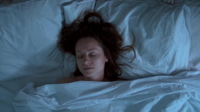Someone pulls  duvet blanket  with sleeping woman at night. She covers her face with horror hands.
